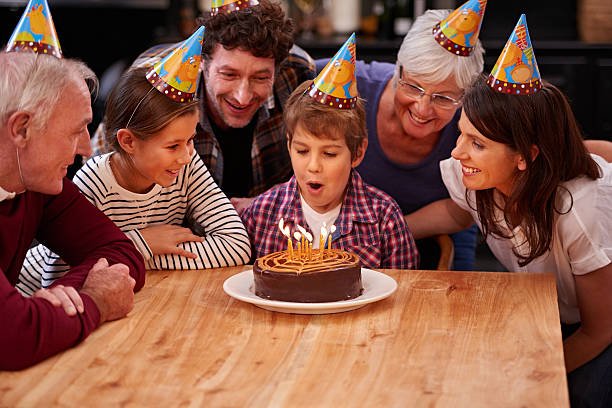 little boy surrounded by family with cake on brown table