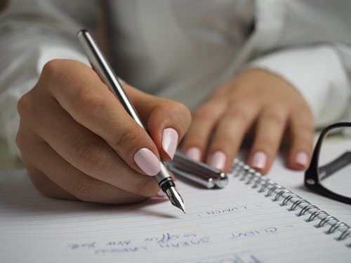 hand holding silver bold pen over book on table