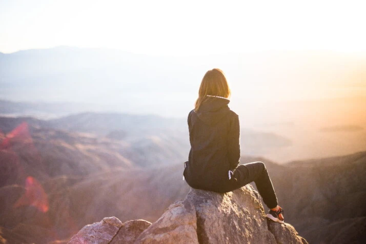 A girl sitting on a rock and watching the sunset.