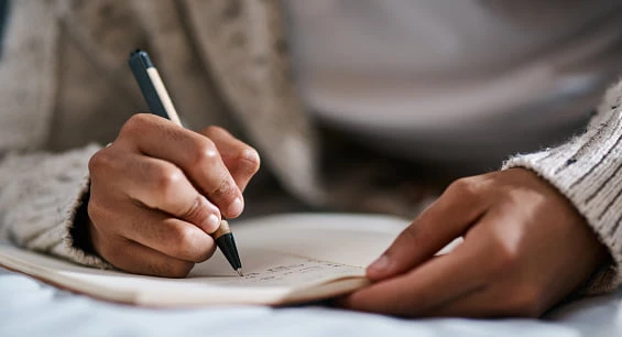 person wearing brown sweater writing with pen in book