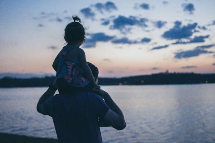 Little girl sitting on father's shoulder and watching the sea. 