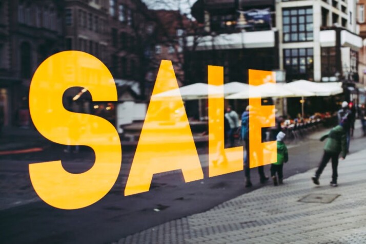 A glass wall on a street that reads sale with yellow letters.