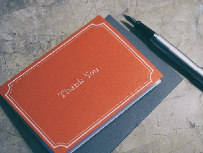 A fountain pen next to a red Thank You card.
