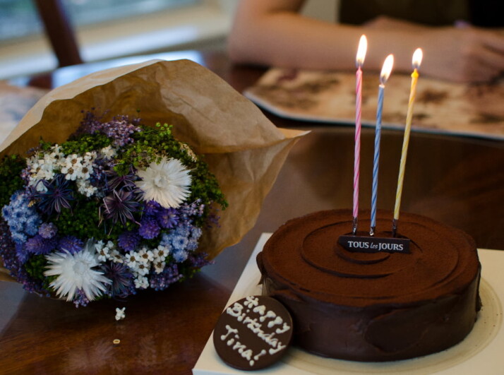A chocolate birthday cake next to a bouquet of beautiful flowers.