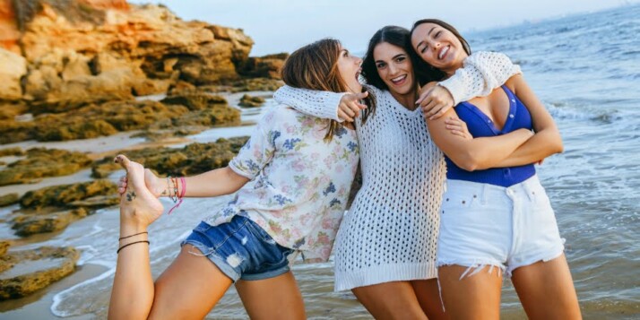 three best friends standing near the beach with hands around each other