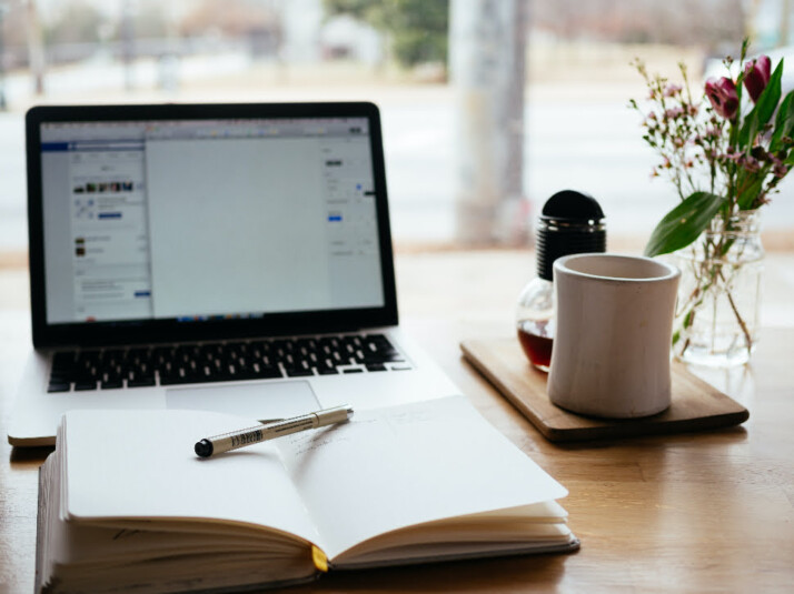 A laptop next to an open notebook and a cup of coffee.
