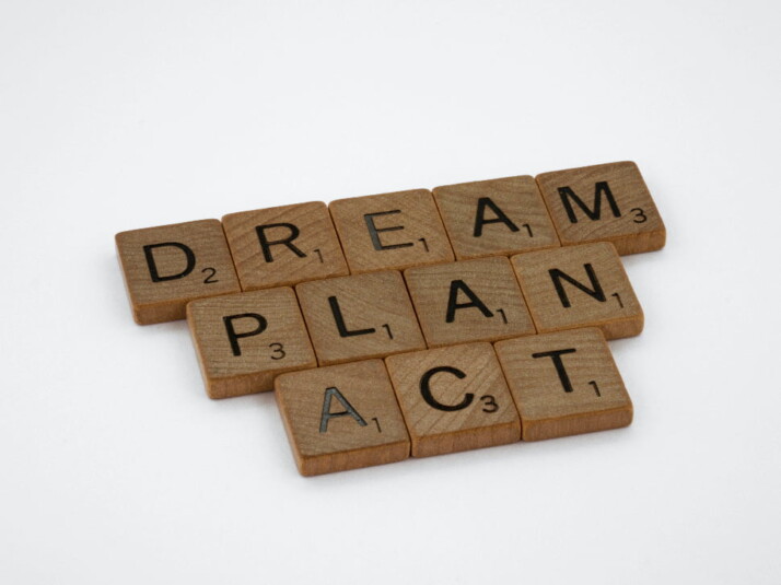 DREAM PLAN ACT brown wooden scrabble blocks on a white background. 