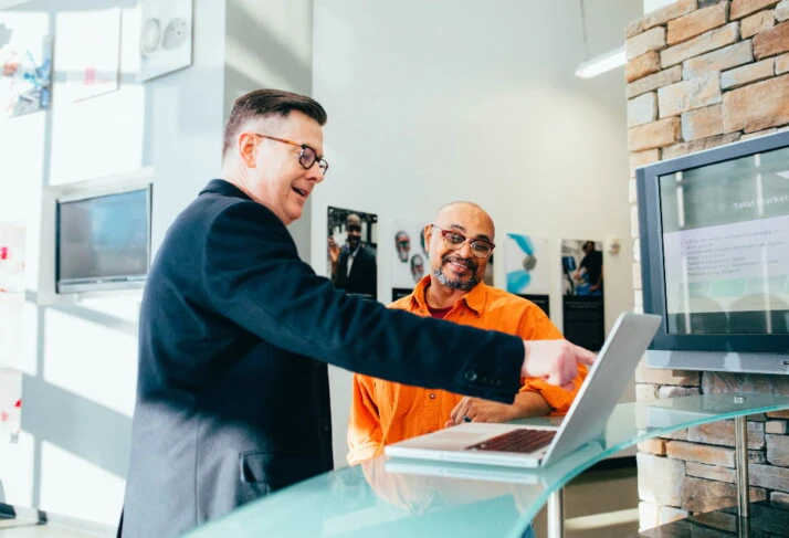  a salesman in an orange shirt showing something to a man in a suit