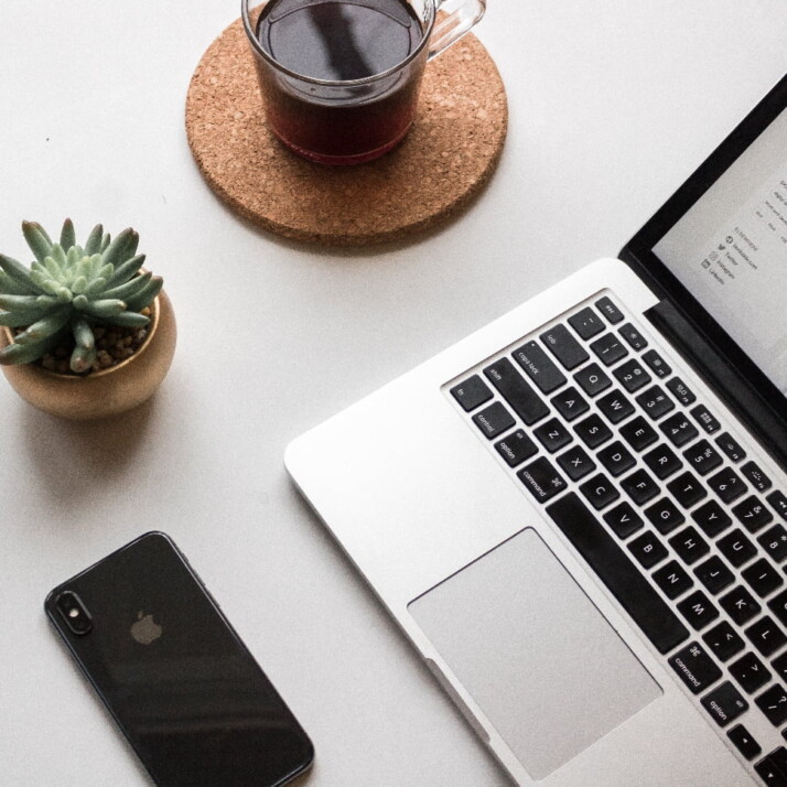 A laptop next to an iPhone, a small succulent, and a cup of coffee.