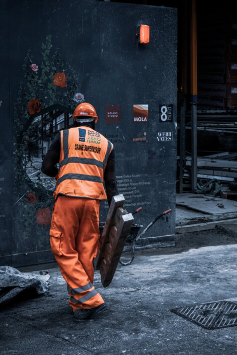 main in orange safety vest that says crane supervisor holding metal.