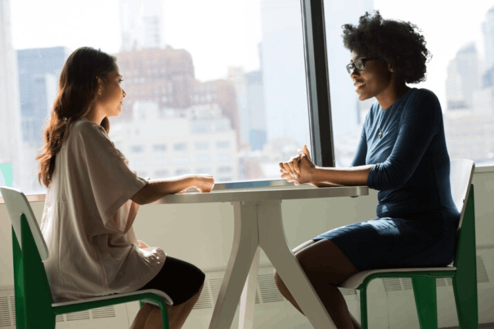 two women sitting beside table and talking about something