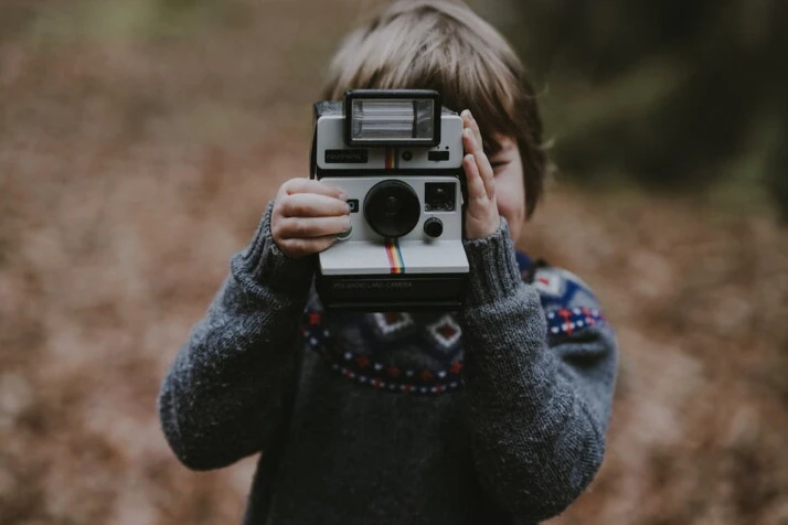 A picture of a boy using white and black instant camera