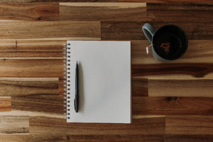 Am open notebook and a pen placed next to a cup of tea.