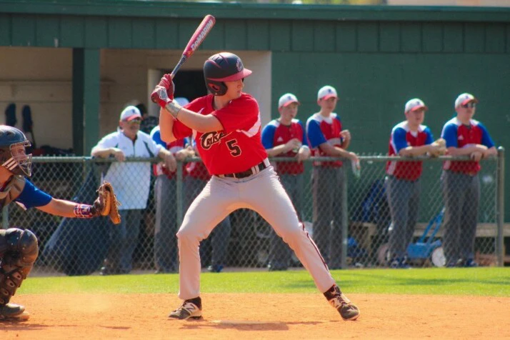 A baseball player in a red jersey hitting the ball. 