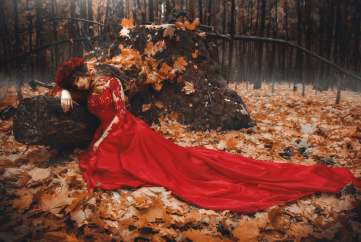 woman in long red dress lying on dried leaves