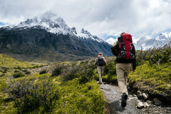 two persons with bag packs walking towards mountain covered with snow