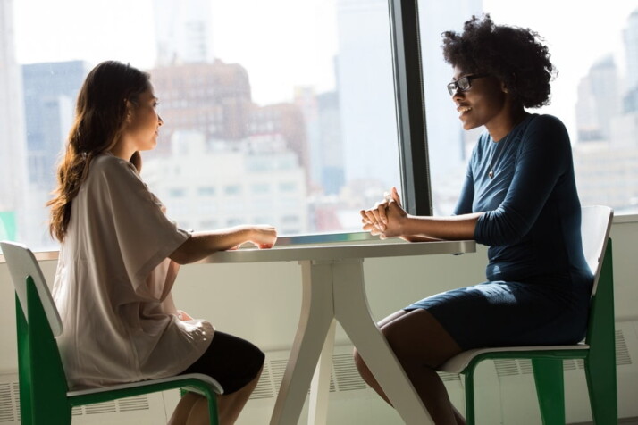 Two women sitting at a table talking as if in an interview.