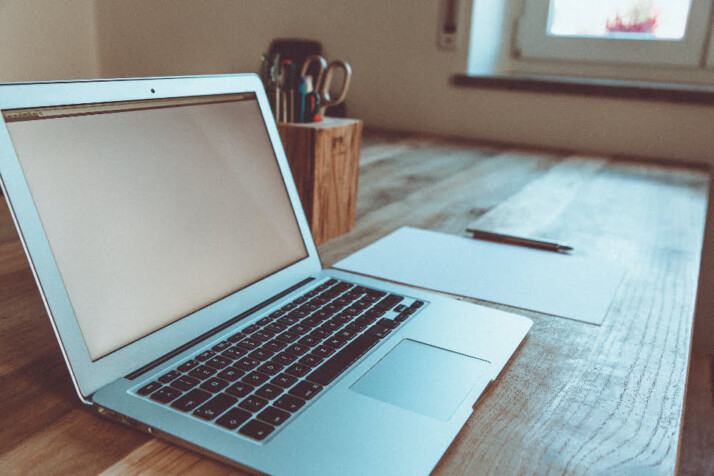 A laptop on top of a table with a pencil and paper next to it.