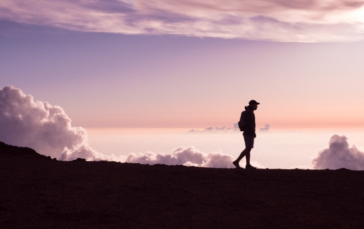 A silhouette of a person walking under white clouds.