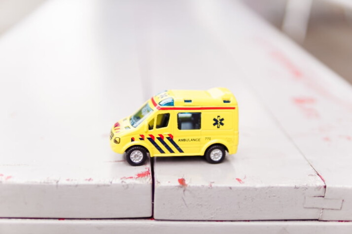 a small yellow toy ambulance on white wooden planks.