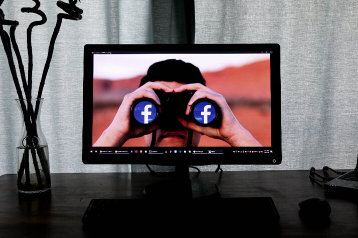 An image of a person using binoculars with the Facebook logo on the lenses.