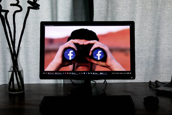 An image of a person using binoculars with the Facebook logo on the lenses.