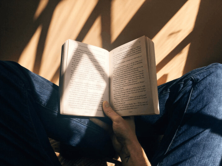 A person holding a book sitting on brown surface