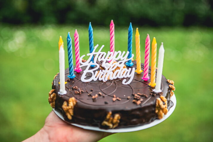 A chocolate cake with a Happy Birthday cake topper and colorful candles.