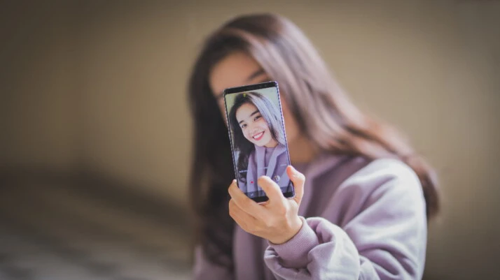A woman wearing a purple jacket taking a selfie on her phone.