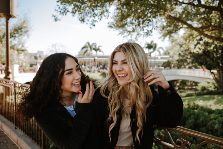 2 women smiling and standing near trees during daytime