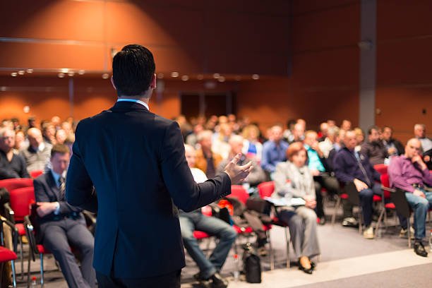 man wearing black suit standing in front of an audience