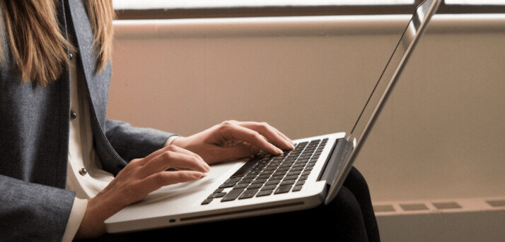 woman wearing white shirt and grey jacket using silver laptop 