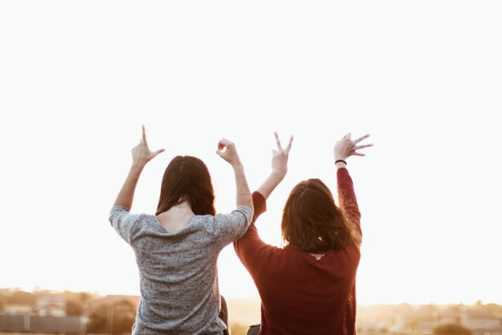 Two women sitting beside each other, holding hand signs up that form the word 