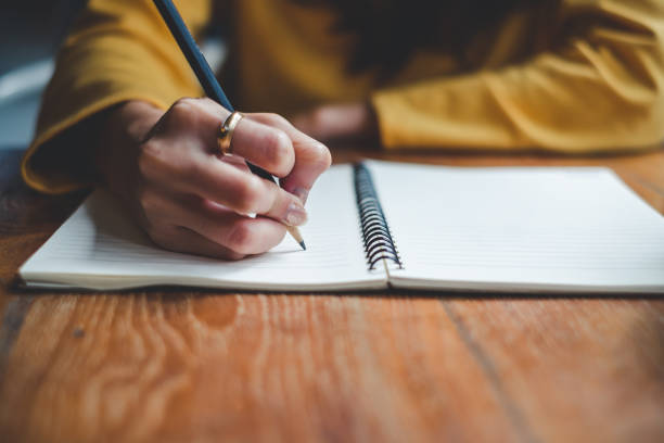 close up woman wearing yellow jacket writing on notebook with hand