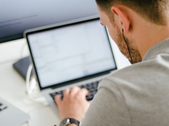 man wearing gray shirt and using ear piece using silver laptop