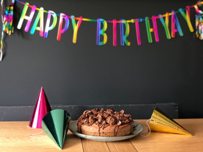 A chocolate cake surrounded by birthday hats and a streamer that says 