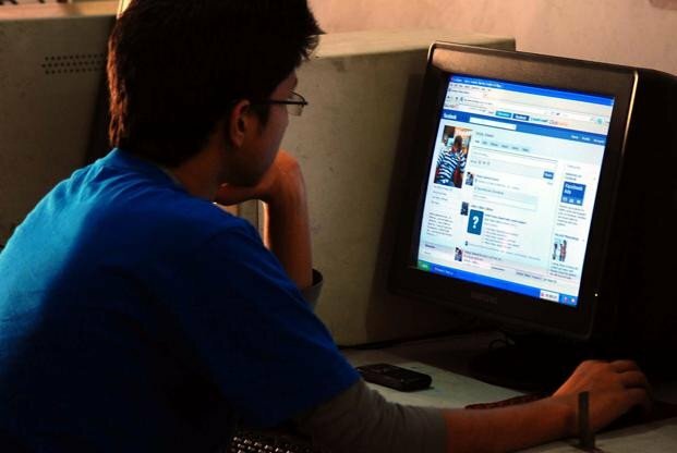 person wearing glasses and blue shirt using desktop computer