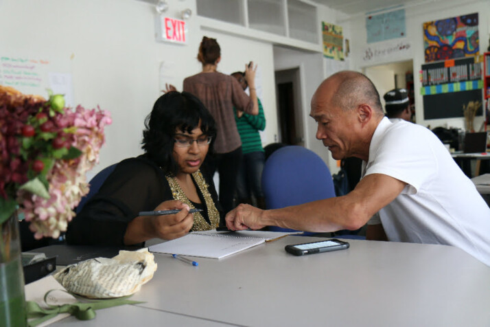 elderly asian man helping a young black or indian woman fill a form.