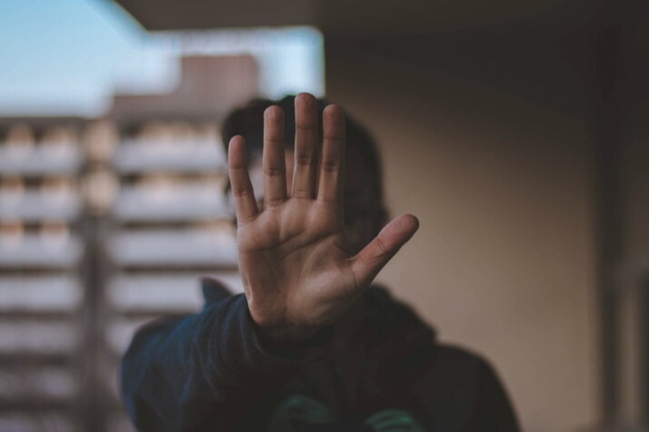 A man standing while wearing black jacket holding his hand up.