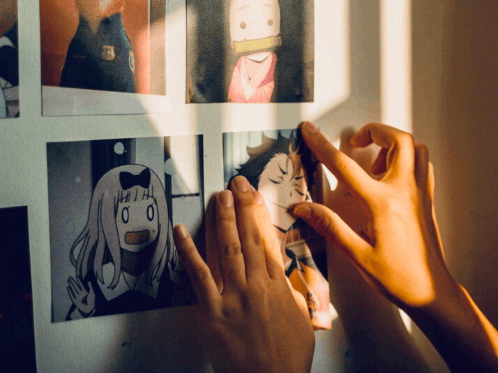 A woman sticking anime pictures on the white wall.