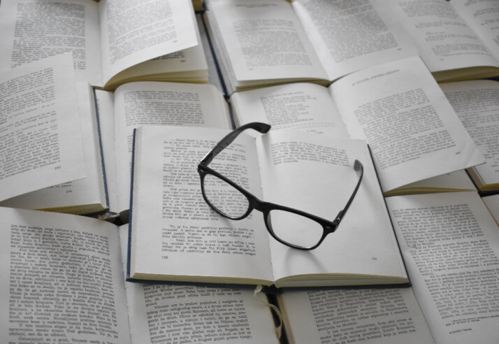 A pair of reading glasses on top of a pile of open books.