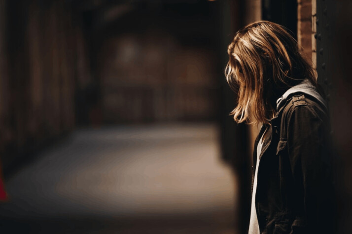 woman with brown hair leaning against a wall in dim hallway