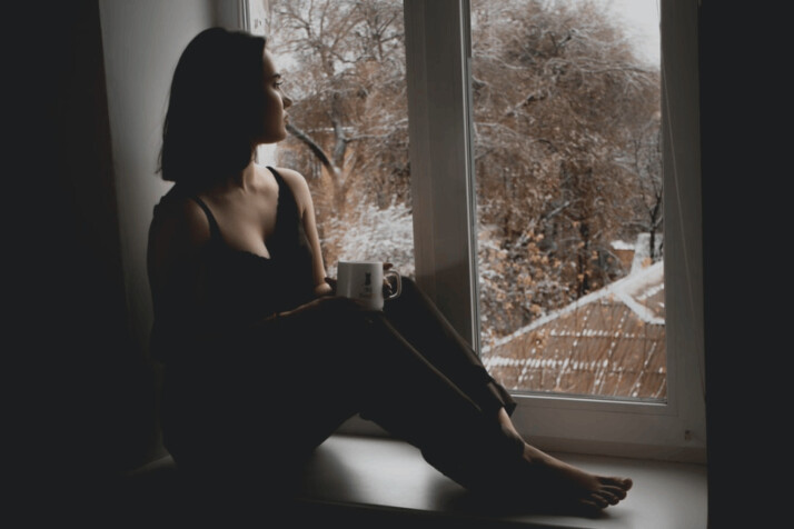woman in black tank top sitting on window with a cup in her hand.