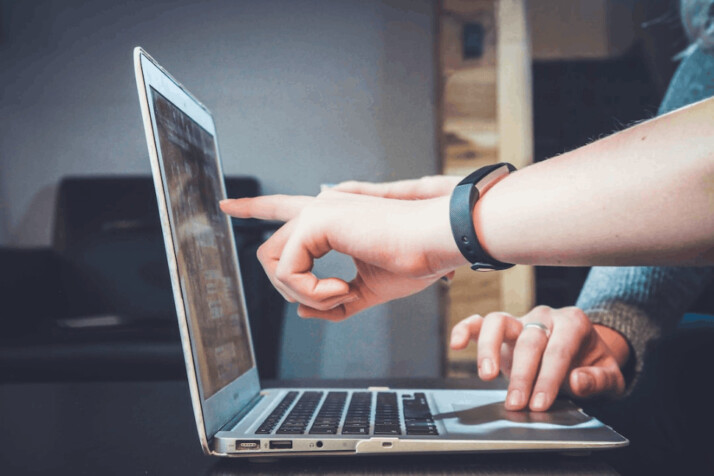 person wearing wristwatch pointing to MacBook Pro laptop screen