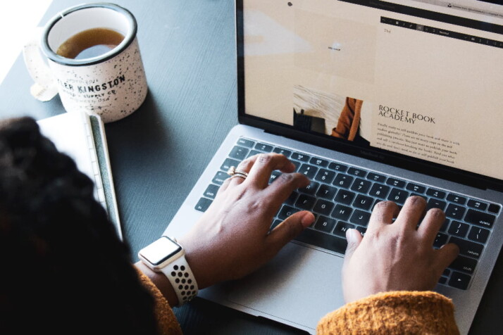 Someone writing a blog on their laptop with a cup of tea on the table.