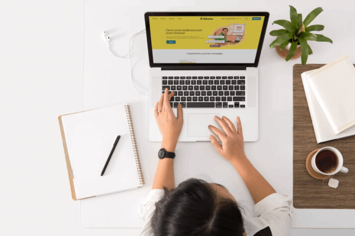 woman using an apple macbook laptop searching something with a notebook and pen beside her