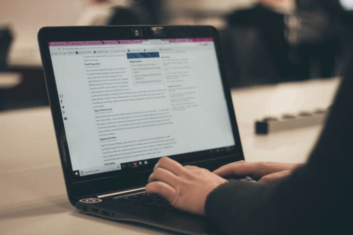 A person in a black garment typing on a laptop computer