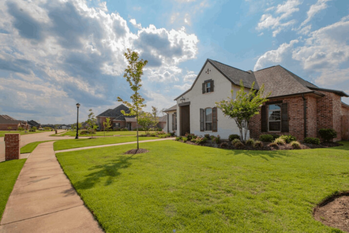 white and brown house near green grass field under white clouds and blue sky.