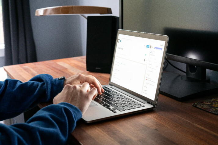 A person working on their laptop on the wooden table.