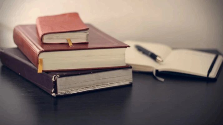 Selective focus photography of three books beside opened notebook